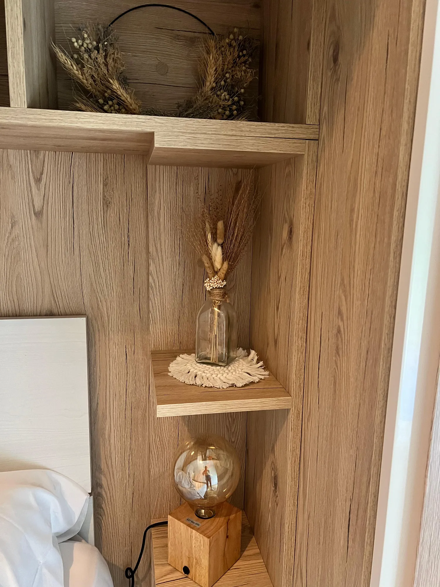 Dettaglio del comodino in rovere del Glam Turin Apartment, con fiori secchi in una bottiglia di vetro e lampada a luce calda